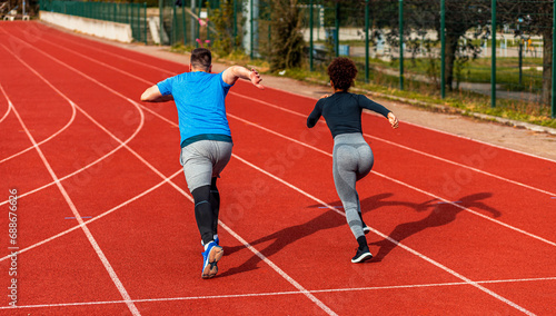Rear view of woman and man doing morning workout outdoors running on track.