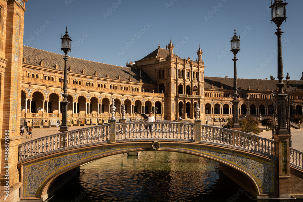 lady on a bridge outside The National Geographic Institute in Plaza de España Seville city Spain. Central government offices in stunning rich wealthy architecture design on sunny day. 