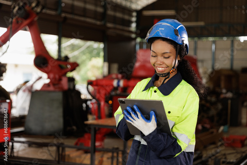 Portrait of female mechanical engineer worker in yellow hard hat and safety uniform using tablet standing at manufacturing area of industrial factory © EKKAPON