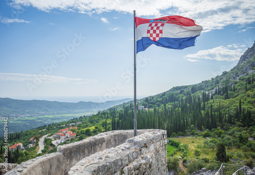 National flag of Croatia on a wall of Sokol fortress on background of green hills grown with cypresses