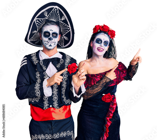 Young couple wearing mexican day of the dead costume over background smiling and looking at the camera pointing with two hands and fingers to the side.