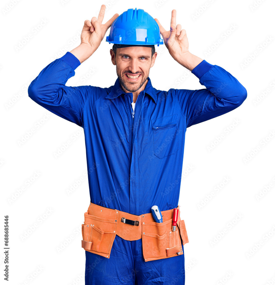 Young handsome man wearing worker uniform and hardhat posing funny and crazy with fingers on head as bunny ears, smiling cheerful Young handsome man wearing worker uniform and hardhat posing funny and crazy with fingers on head as bunny ears, smiling cheerful