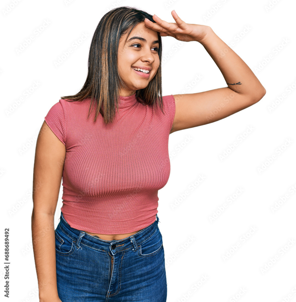 Young hispanic girl wearing casual t shirt very happy and smiling looking far away with hand over head. searching concept. Young hispanic girl wearing casual t shirt very happy and smiling looking far away with hand over head. searching concept.