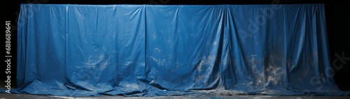 A tarpaulin laid out on a floor speckled with drips of blue paint, the upper part of the frame vacated for descriptive text.