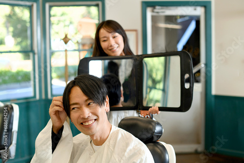 男性客に鏡を見せる美容師のアジア人女性 photo