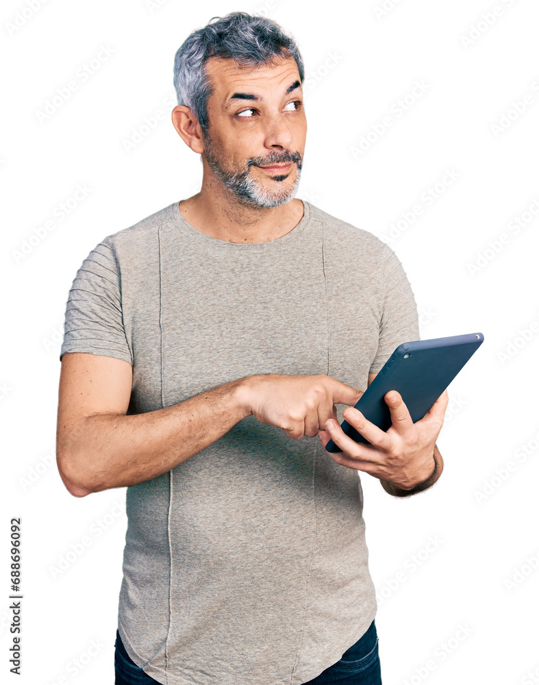 Middle age hispanic with grey hair using touchpad device smiling looking to the side and staring away thinking. Middle age hispanic with grey hair using touchpad device smiling looking to the side and staring away thinking.