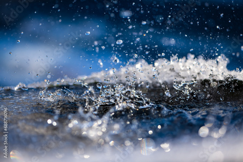 Water splashing into a rain barrel rimmed with ice crystals. Vivid water surface with drops, bubbles, waves and splashes backlit by contrasting sunlight. Close up with selective focus and motion.