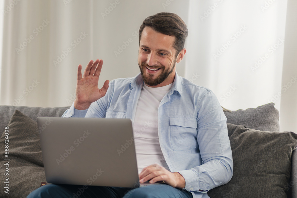Man entrepreneur freelancer uses a laptop for work, having online meeting while sitting on the couch at home Man entrepreneur freelancer uses a laptop for work, having online meeting while sitting on the couch at home