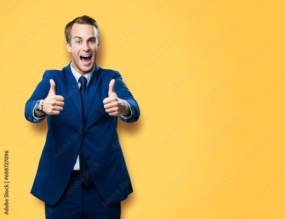 Happy excited businessman showing two thumbs up like hand gesture, in blue confident suit, against vivid yellow background. Very cheerful man. Copy space for ad, slogan or text. Happy excited businessman showing two thumbs up like hand gesture, in blue confident suit, against vivid yellow background. Very cheerful man. Copy space for ad, slogan or text.