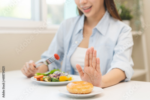 Diet concept, close up young woman, girl using hand push out, stop sweet donut, dessert or junk food on plate, choose green vegetables salad, eat low fat for good health. Female getting weight loss.