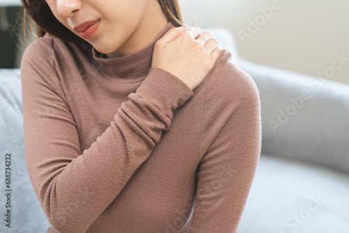 Pain body muscles stiff problem, suffer asian young woman, girl face painful, hand holding neck ache from work hand holding massaging rubbing shoulder hurt, sore sitting on couch at home. Health care photo
