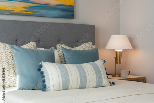 Relaxing bedroom detail of blue and white pillows on bed with gray headboard and decorative gold side lamp. photo