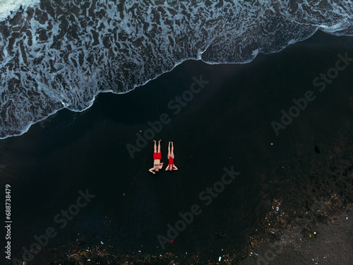 Black sand beach. Fantastic landscape of black sand volcano Ureki beach in Georgia. Couple having a good time on vacation. A man and a woman in red swimsuits are lying down