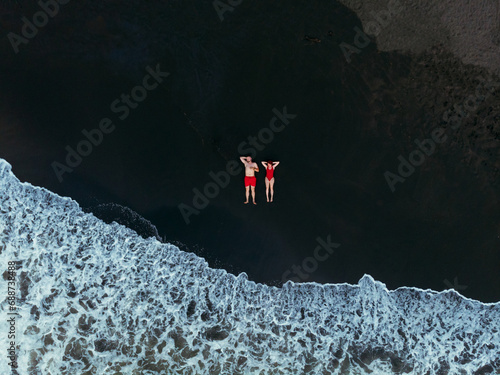 Black sand beach. Fantastic landscape of black sand volcano Ureki beach in Georgia. Couple having a good time on vacation. A man and a woman in red swimsuits are lying down