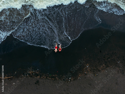 Black sand beach. Fantastic landscape of black sand volcano Ureki beach in Georgia. Couple having a good time on vacation. A man and a woman in red swimsuits are lying down. Garbage after the storm
