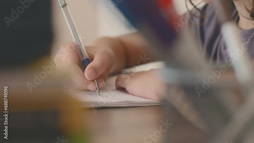 Side view of a concentrated little boy learning to write while doing his homework while sitting at his desk at home. hand close up. Portrait of a smart preschooler who is learning to write.
 photo