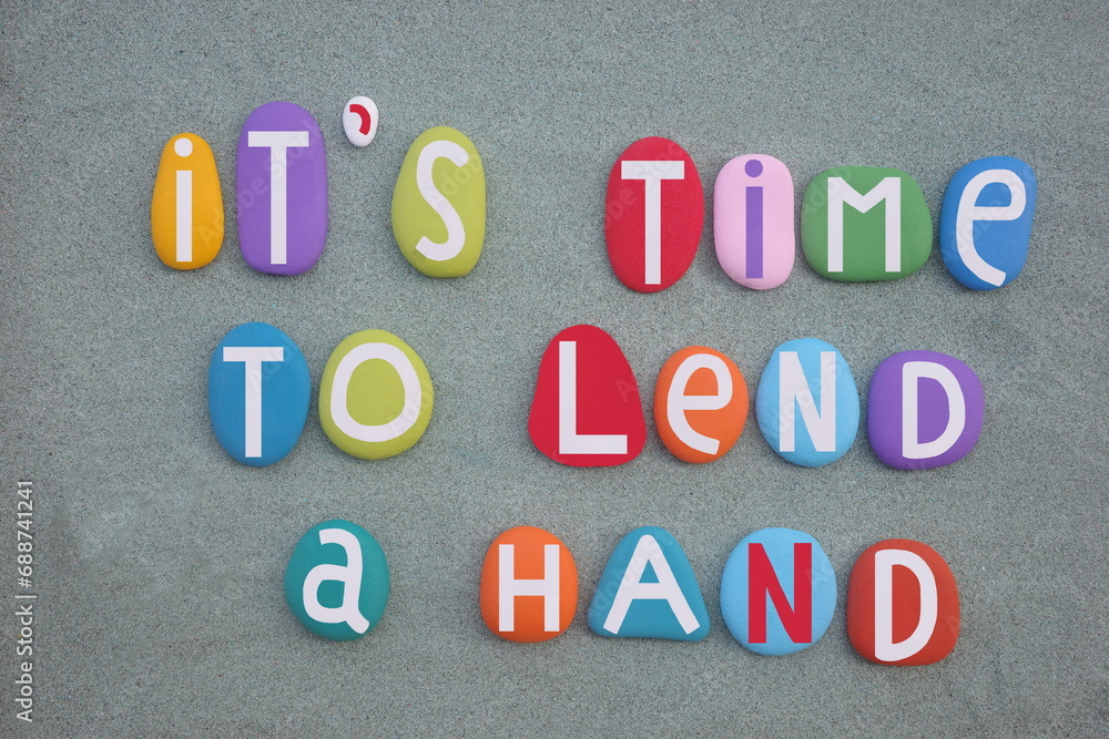 It is time to lend a hand, social slogan composed with hand painted multi colored stone letters over green sand It is time to lend a hand, social slogan composed with hand painted multi colored stone letters over green sand