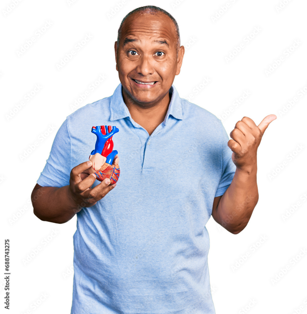 Hispanic middle age man holding heart organ pointing thumb up to the side smiling happy with open mouth Hispanic middle age man holding heart organ pointing thumb up to the side smiling happy with open mouth