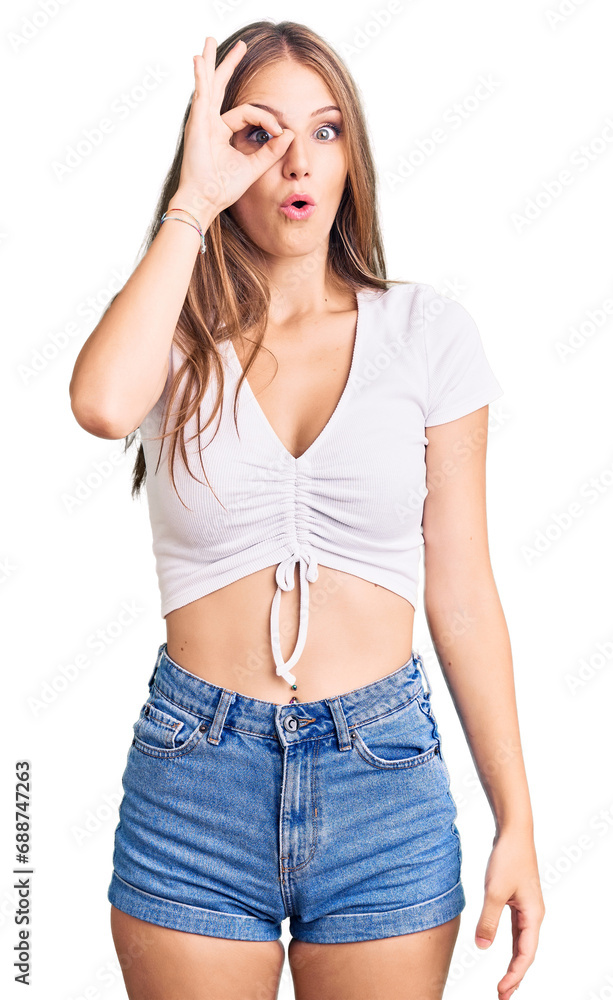 Young beautiful blonde woman wearing casual white tshirt doing ok gesture shocked with surprised face, eye looking through fingers. unbelieving expression. Young beautiful blonde woman wearing casual white tshirt doing ok gesture shocked with surprised face, eye looking through fingers. unbelieving expression.
