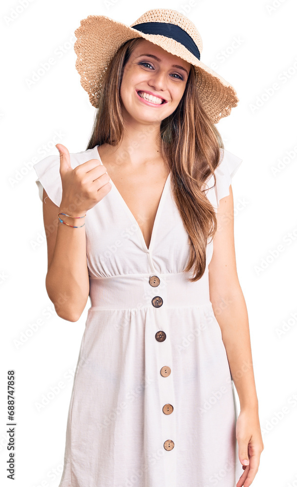 Young beautiful blonde woman wearing summer dress and hat doing happy thumbs up gesture with hand. approving expression looking at the camera showing success. Young beautiful blonde woman wearing summer dress and hat doing happy thumbs up gesture with hand. approving expression looking at the camera showing success.
