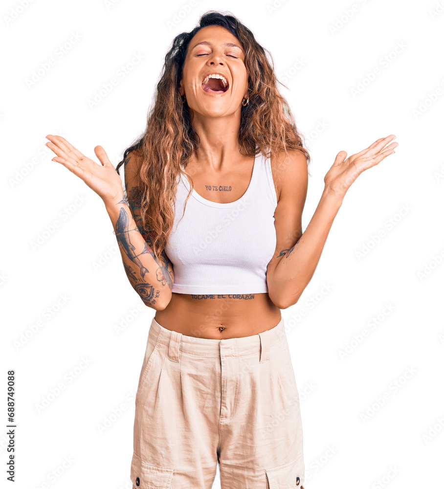 Young hispanic woman with tattoo wearing casual clothes celebrating mad and crazy for success with arms raised and closed eyes screaming excited. winner concept Young hispanic woman with tattoo wearing casual clothes celebrating mad and crazy for success with arms raised and closed eyes screaming excited. winner concept