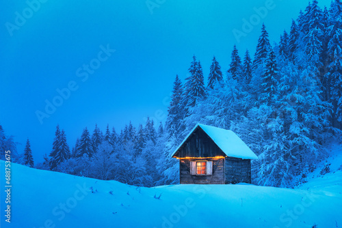 A lonely wooden house surrounded by snowy pine trees in a mountain glade deep within the woods in a wintery landscape. Christmas holiday postcard. Snowy mountains forest