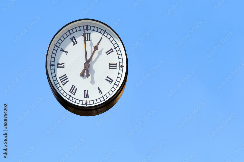Street round clock with Roman numerals on a blue clear sky Street round clock with Roman numerals on a blue clear sky