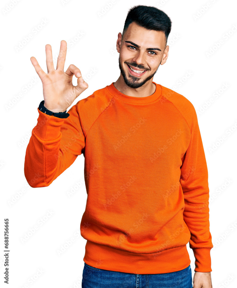 Young hispanic man with beard wearing casual orange sweater smiling positive doing ok sign with hand and fingers. successful expression. Young hispanic man with beard wearing casual orange sweater smiling positive doing ok sign with hand and fingers. successful expression.