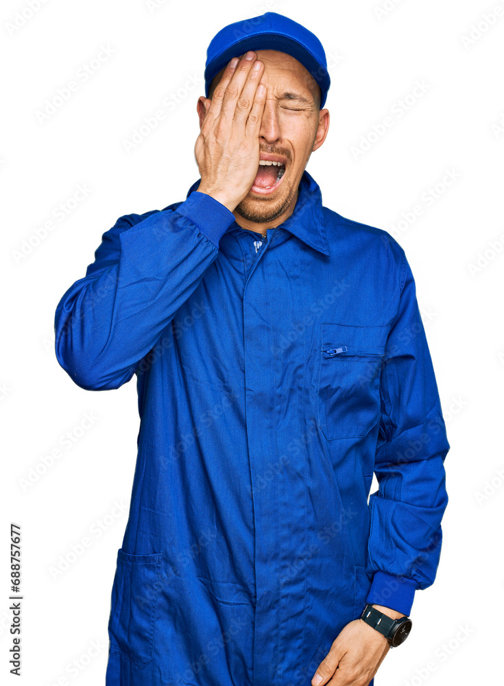Bald man with beard wearing builder jumpsuit uniform yawning tired covering half face, eye and mouth with hand. face hurts in pain. Bald man with beard wearing builder jumpsuit uniform yawning tired covering half face, eye and mouth with hand. face hurts in pain.