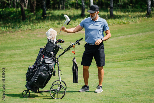 Professional older golfer takes one of clubs out of bag playing outdoors