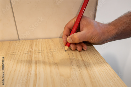 Marking a worktop with a lead pencil. The carpenter prepares the wooden part to saw it. Building a new kitchen in an apartment. Working at home with DIY equipment.
