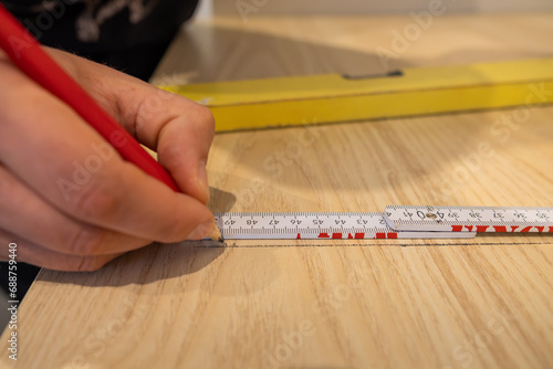 Marking a line with a pencil to saw the worktop board in a new kitchen. Carpenter working to renovate the furniture in an apartment. Using a folding rule to measure the length.