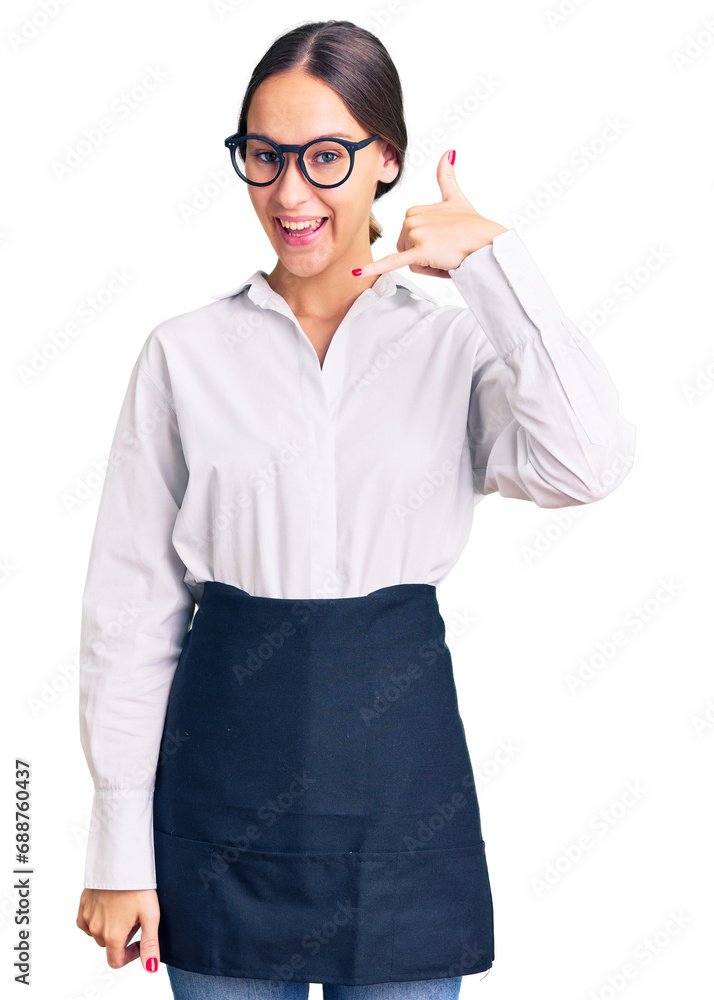 Beautiful brunette young woman wearing professional waitress apron smiling doing phone gesture with hand and fingers like talking on the telephone. communicating concepts. Beautiful brunette young woman wearing professional waitress apron smiling doing phone gesture with hand and fingers like talking on the telephone. communicating concepts.