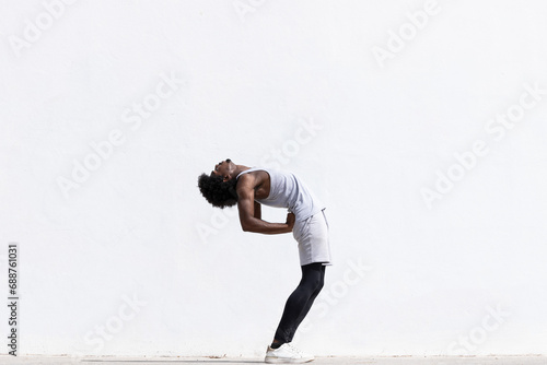 Black athlete stretching body over white wall photo