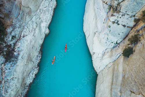 High angle view of unrecognizable people kayaking on blue narrow river flowing between rocky mountains during vacation at daytime photo