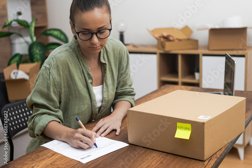 A young lady, seated at her home table, meticulously completes a return order form, articulating her intention to return a purchased item.  photo