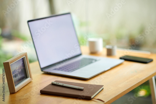 Planner and pen next to laptop on home office desk in room with huge windows