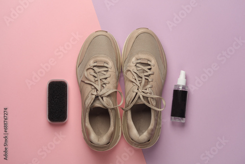 Sneakers with sponge and spray bottle on pink background. Shoe care. Top view. Flat lay