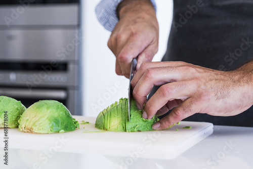 Closeup of Crop unrecognizable chef in apron slicing avocado with knife on cutting board photo
