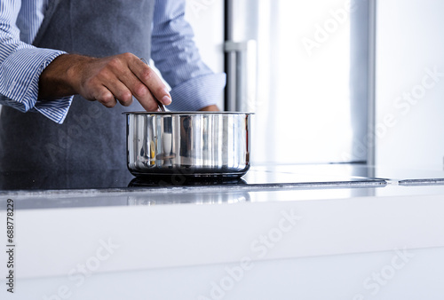Crop anonymous man chef in apron standing and stirring ingredients in pan near kitchen table in daytime photo
