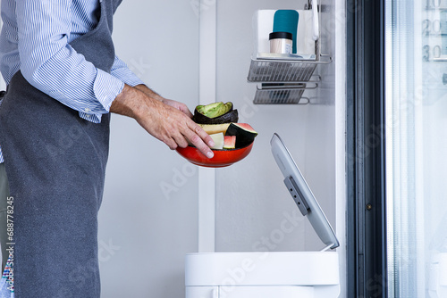 Unrecognizable man chef in apron standing with fruits waste near automatic trash bin photo