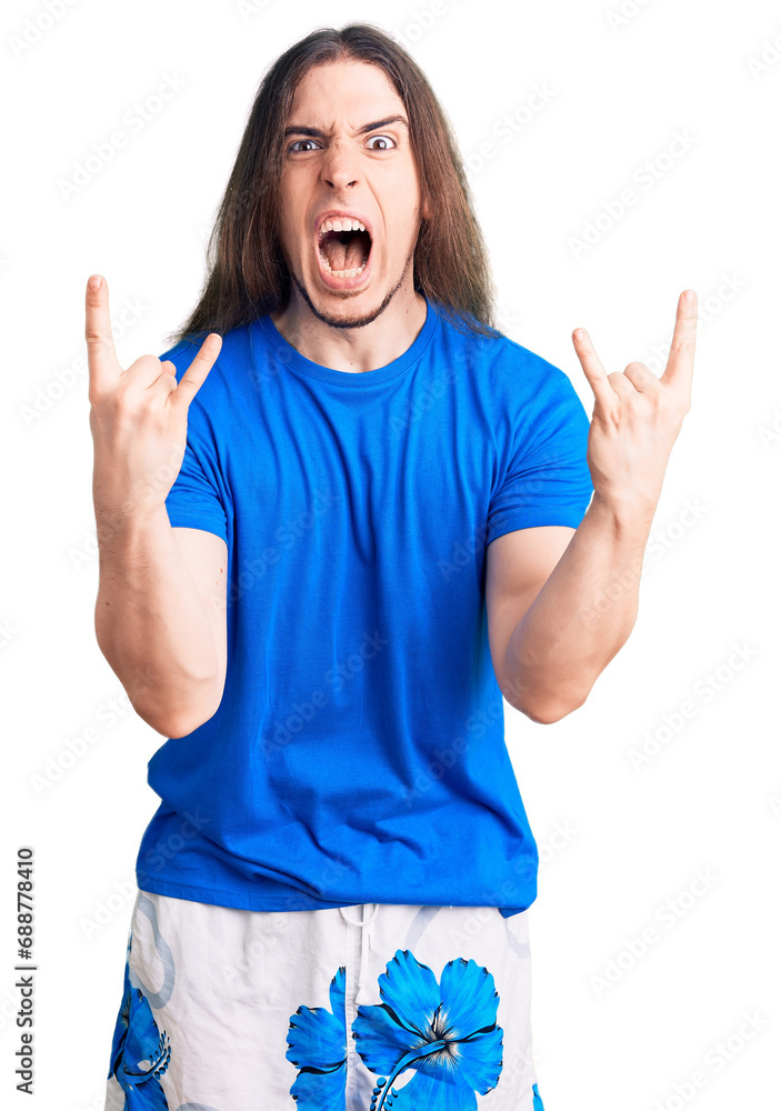 Young adult man with long hair wearing swimwear shouting with crazy expression doing rock symbol with hands up. music star. heavy concept. Young adult man with long hair wearing swimwear shouting with crazy expression doing rock symbol with hands up. music star. heavy concept.