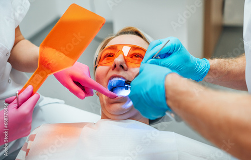 Photography Young woman in protective eyeglasses during teeth composite filling material polymerization procedure with curing UV light at dentist's office