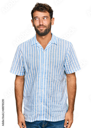 Handsome young man with beard wearing casual fresh shirt smiling looking to the side and staring away thinking.