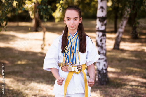 Young girl wearing karate fighter uniform and medals holding trophy. Karateka champion