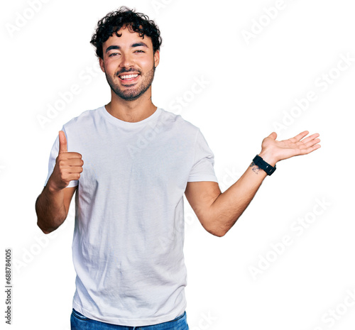 Hispanic young man with beard wearing casual white t shirt showing palm hand and doing ok gesture with thumbs up, smiling happy and cheerful photo