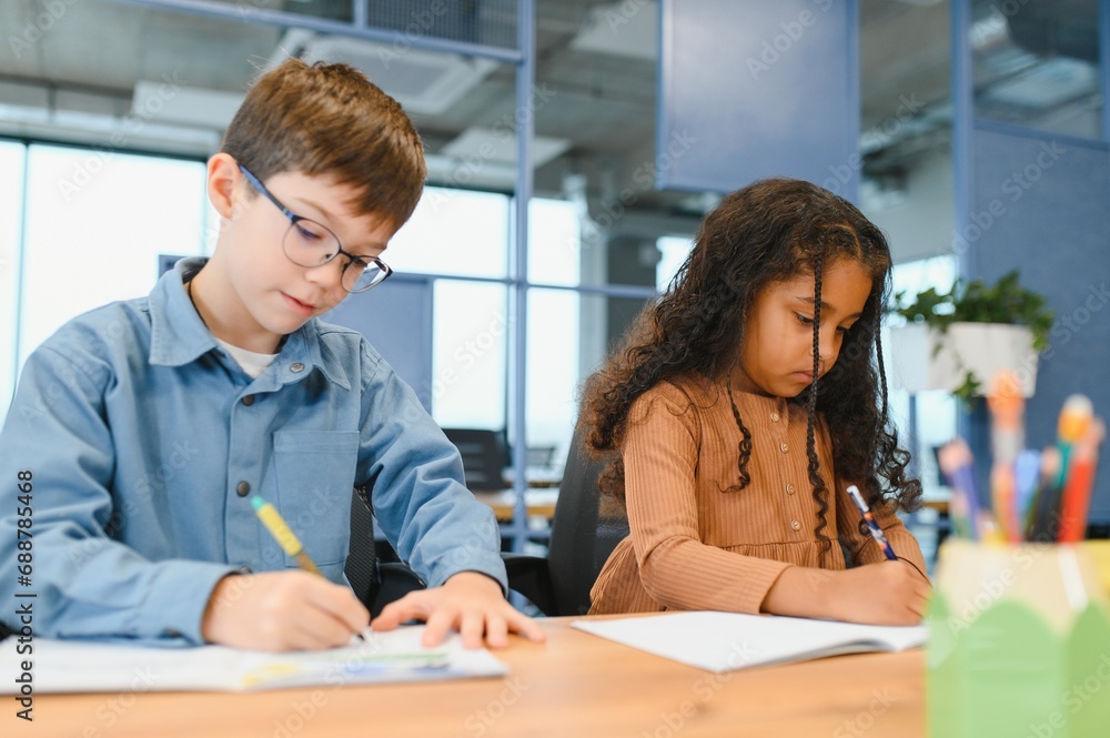 Focused multiracial students kids writing down data into notebook while sitting at table Focused multiracial students kids writing down data into notebook while sitting at table
