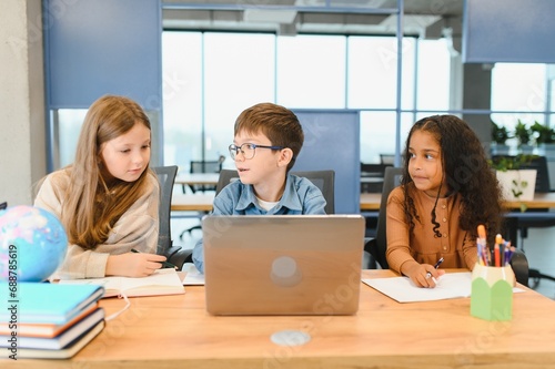 Portrait of smart schoolgirls and schoolboys looking at the laptop in classroom
