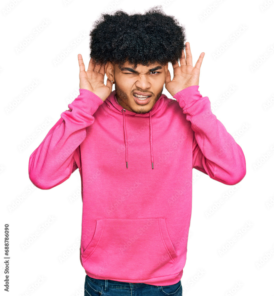 Young african american man with afro hair wearing casual pink sweatshirt trying to hear both hands on ear gesture, curious for gossip. hearing problem, deaf Young african american man with afro hair wearing casual pink sweatshirt trying to hear both hands on ear gesture, curious for gossip. hearing problem, deaf
