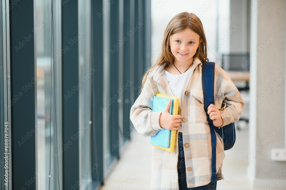 little beautiful school girl standing among corridor at school, holding notes at hands. Funny and happy girl smiling at camera, resting after lessons on primary school little beautiful school girl standing among corridor at school, holding notes at hands. Funny and happy girl smiling at camera, resting after lessons on primary school